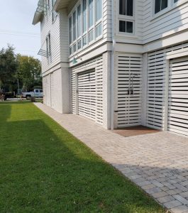 Two-story white house with slatted garage doors, large windows, and a paved driveway beside a green lawn.