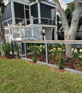 A modern house with a screened porch, raised deck, and a fenced garden with flowers and small shrubs in the yard.