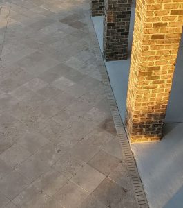 Brick columns cast shadows on a tiled stone patio in warm sunlight.