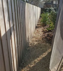 A narrow gravel path runs alongside a wooden fence with some plants and trees visible on the right side.