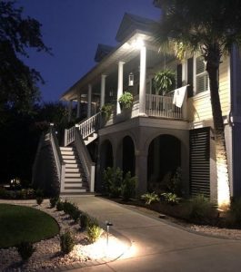 Two-story house with a front porch, outdoor staircase, and driveway at dusk, illuminated by exterior lights.