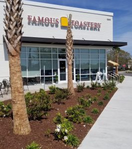 Exterior view of Famous Toastery restaurant with outdoor seating, palm trees, and landscaped walkway.