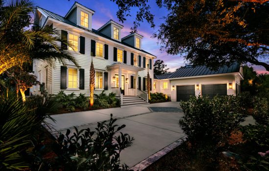 Two Story home with white siding, featuring lit windows and landscape lighting