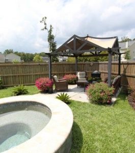 Backyard with a small round pool, green lawn, seating area under a pergola, and wooden fence surrounding the yard.