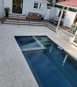 Modern backyard with a rectangular swimming pool, tiled patio, wooden deck, outdoor seating, and dining area.