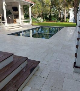Outdoor patio with stone tile flooring, a small rectangular pool, wooden steps, and a covered dining area.